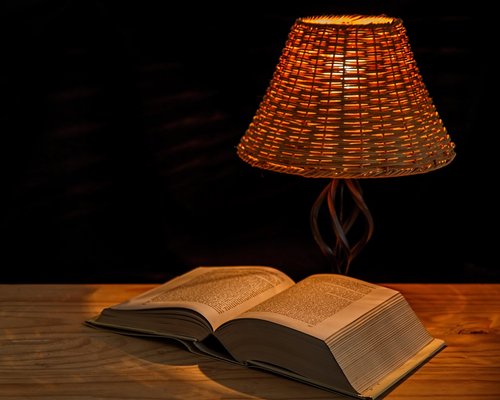 Warm desk lamp illuminating a book page with soft light in a dim room